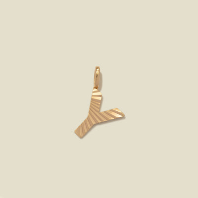 A small gold Y-shaped charm with a textured, sunburst striped pattern, shown on a solid light beige background.