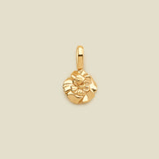 A polished yellow gold flower charm pendant with a textured, layered petal design and a top loop, centered on a solid light beige background.