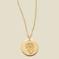 A gold chain necklace with a round gold disc pendant featuring an engraved carnation flower design, displayed against a solid light beige background.