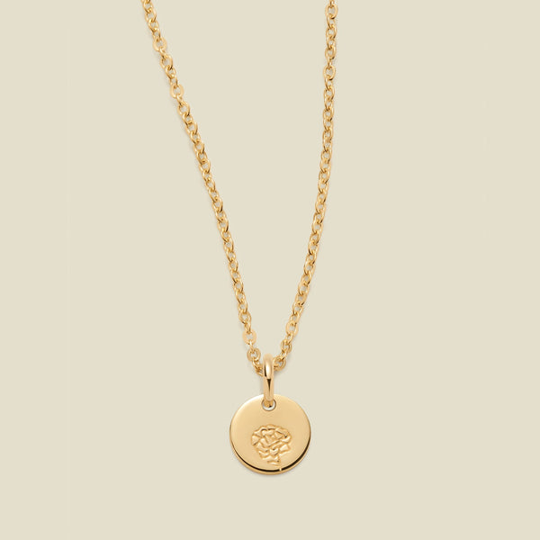 A gold chain necklace with a round gold disc pendant featuring an engraved carnation flower design, displayed against a solid light beige background.