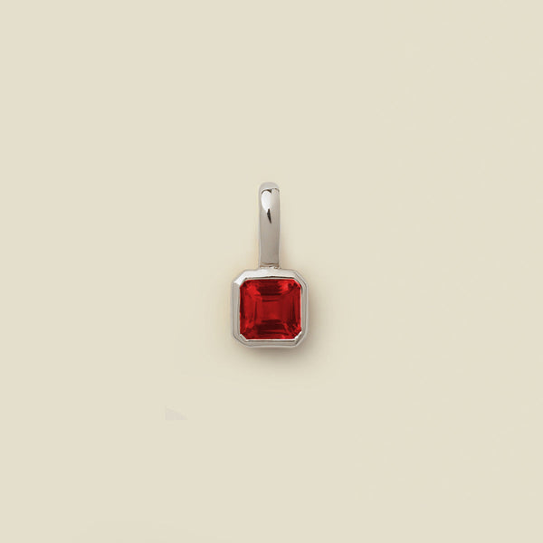 A square-cut red gemstone pendant in a polished silver bezel setting, centered on a solid light beige background.