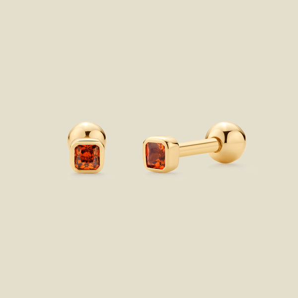 A pair of gold post earrings with square-cut red-orange gemstones, shown from front and side angles on a light beige background.