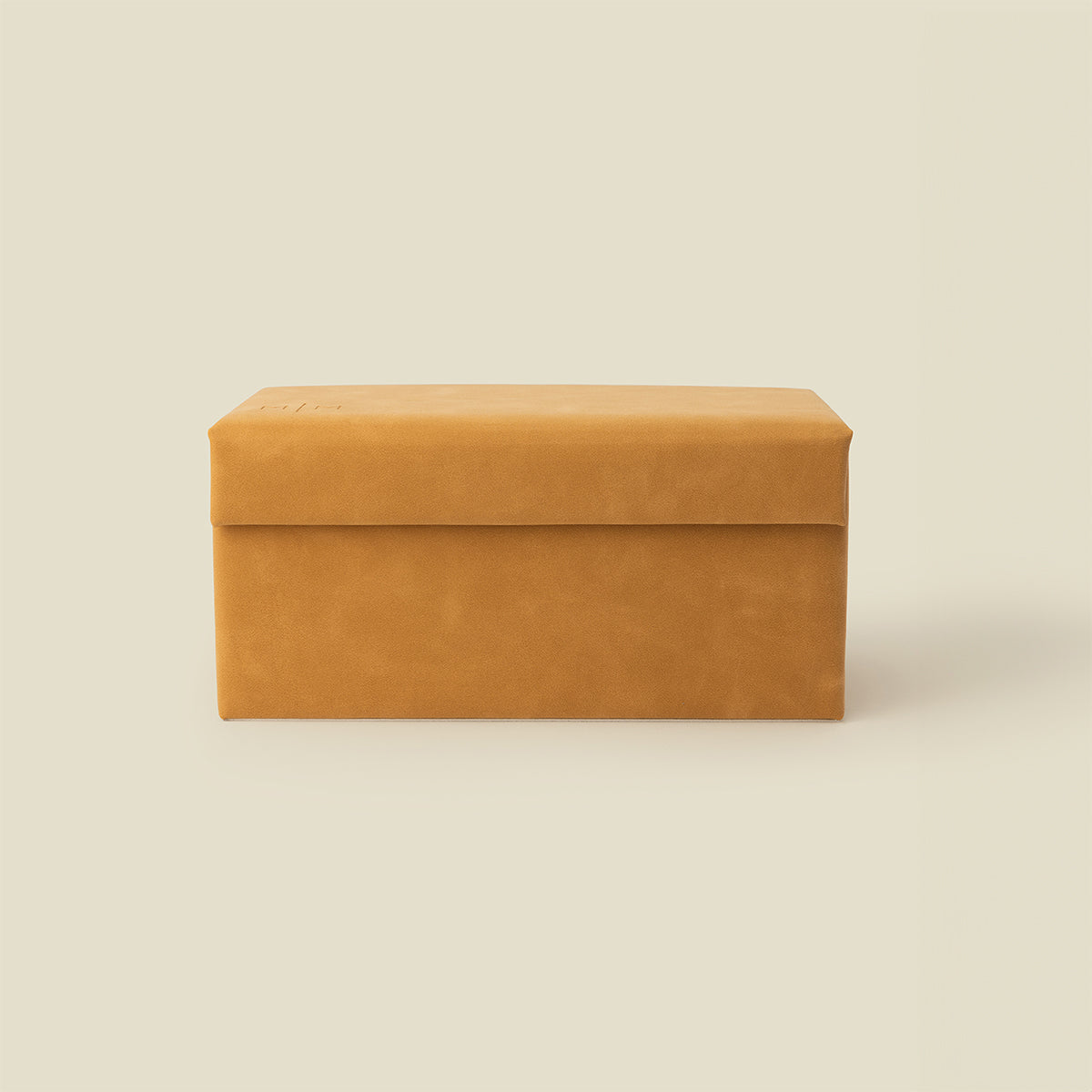 A rectangular tan leather storage box with a hinged lid, shown against a solid light beige background.