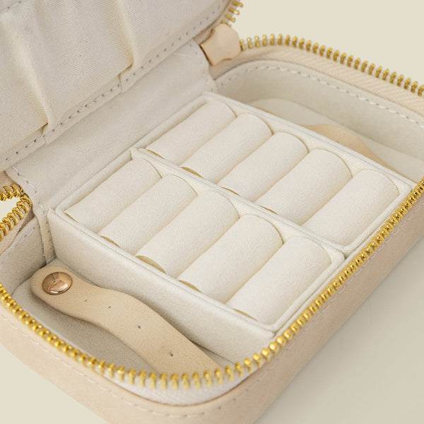 An open cream-colored jewelry organizer case with a gold zipper and white interior compartments, shown on a solid light beige background.