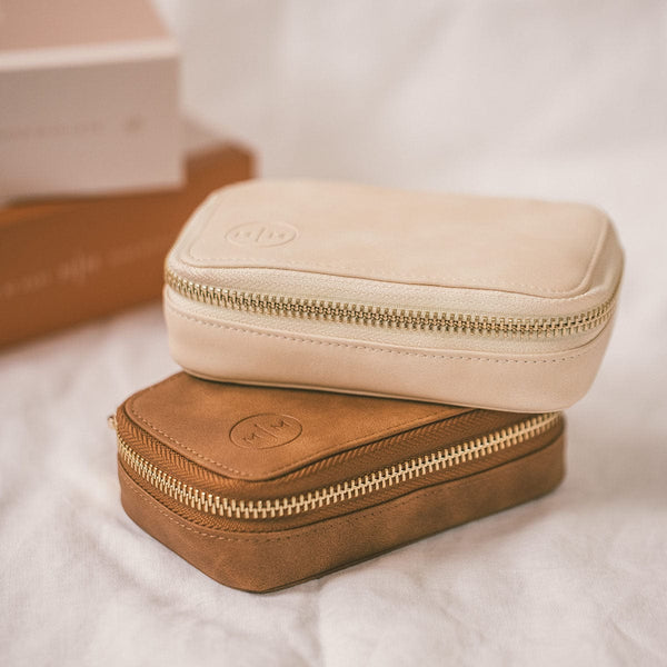Two rectangular zippered pouches stacked on a marbled white surface. The top pouch is light beige with a gold zipper, and the bottom pouch is medium brown with a gold zipper.