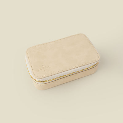 A rectangular cream colored jewelry case with a gold zipper, shown on a solid light beige background.