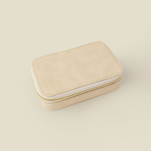 A rectangular cream colored jewelry case with a gold zipper, shown on a solid light beige background.