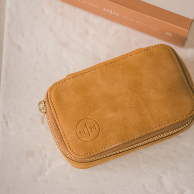 A rectangular tan leather jewelry case with a gold zipper, shown on a white marbled surface.