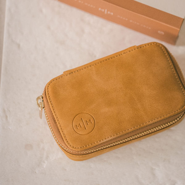 A rectangular tan leather jewelry case with a gold zipper, shown on a white marbled surface.