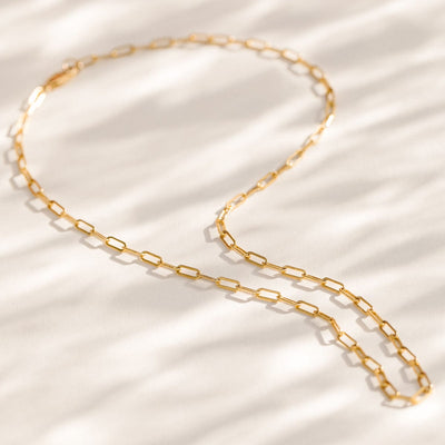 A gold paperclip link chain necklace laying on a textured white surface.