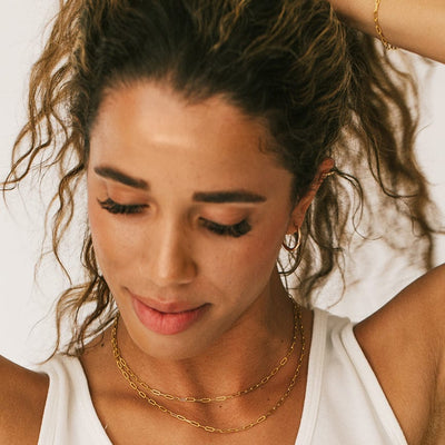 A person holding up their hair, showcasing two gold paperclip link chain necklaces around their neck.