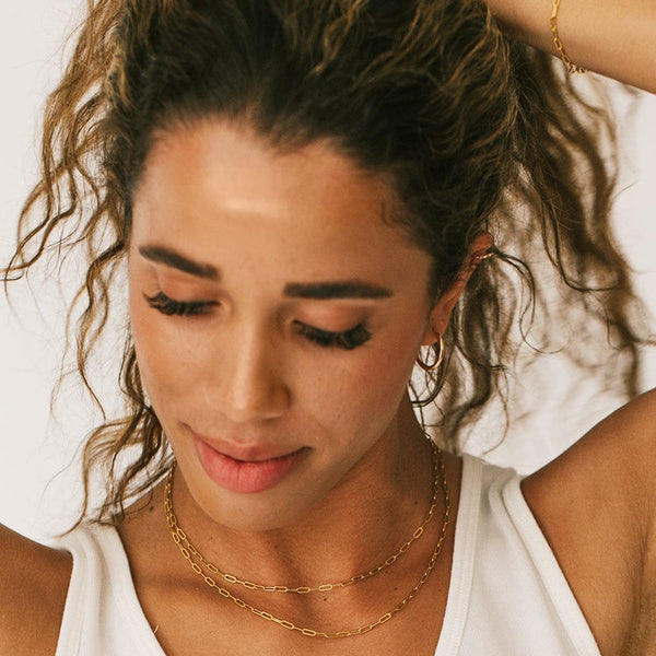 A person holding up their hair, showcasing two gold paperclip link chain necklaces around their neck.