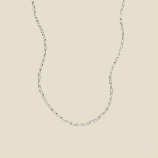 A silver paperclip chain necklace draped in a U-shape against a solid beige background.