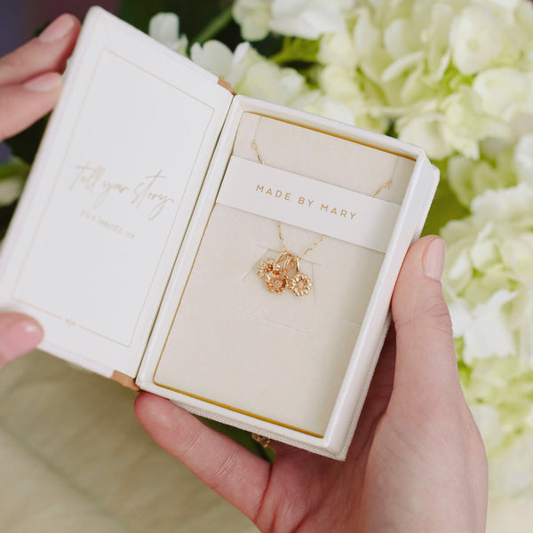 A cream colored jewelry box held open with a gold pendant chain necklace holding three small flower charms.