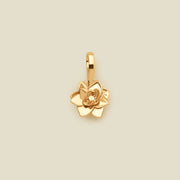 A polished gold lotus flower charm, shown against a solid light beige background.