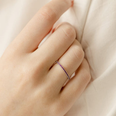 A close-up of a hand resting on a cream cloth with a thin silver ring, featuring a single row of small dark red gemstones across the front.