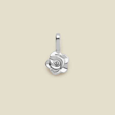 A small polished silver rose flower charm, shown on a solid light beige background.
