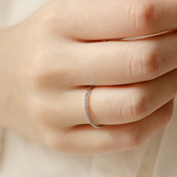A close-up of a hand with a thin silver ring, featuring a single row of small light purple gemstones.