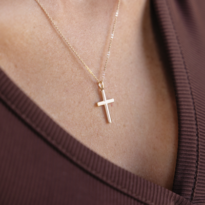 Gold cross necklace on a person wearing a brown garment