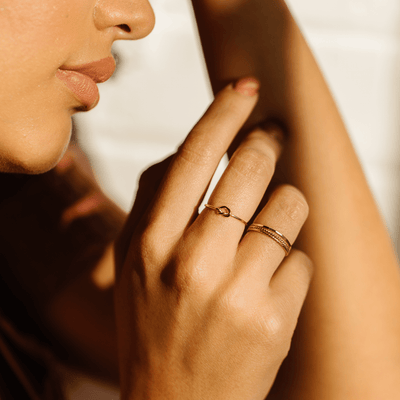 A person's hands in warm sunlight, showcasing multiple thin gold wire rings.