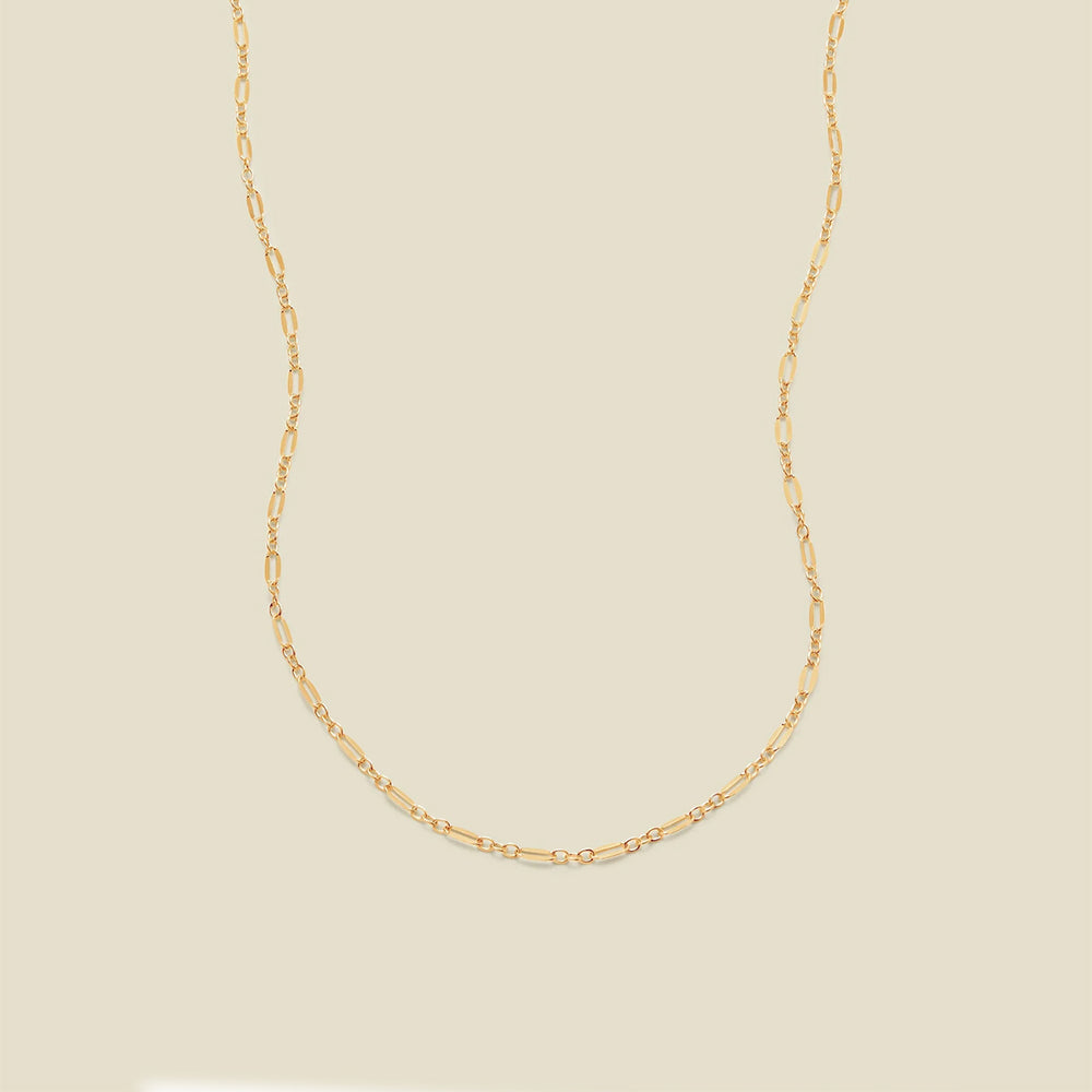 A delicate gold chain necklace with elongated oval links, displayed against a solid, warm beige background.