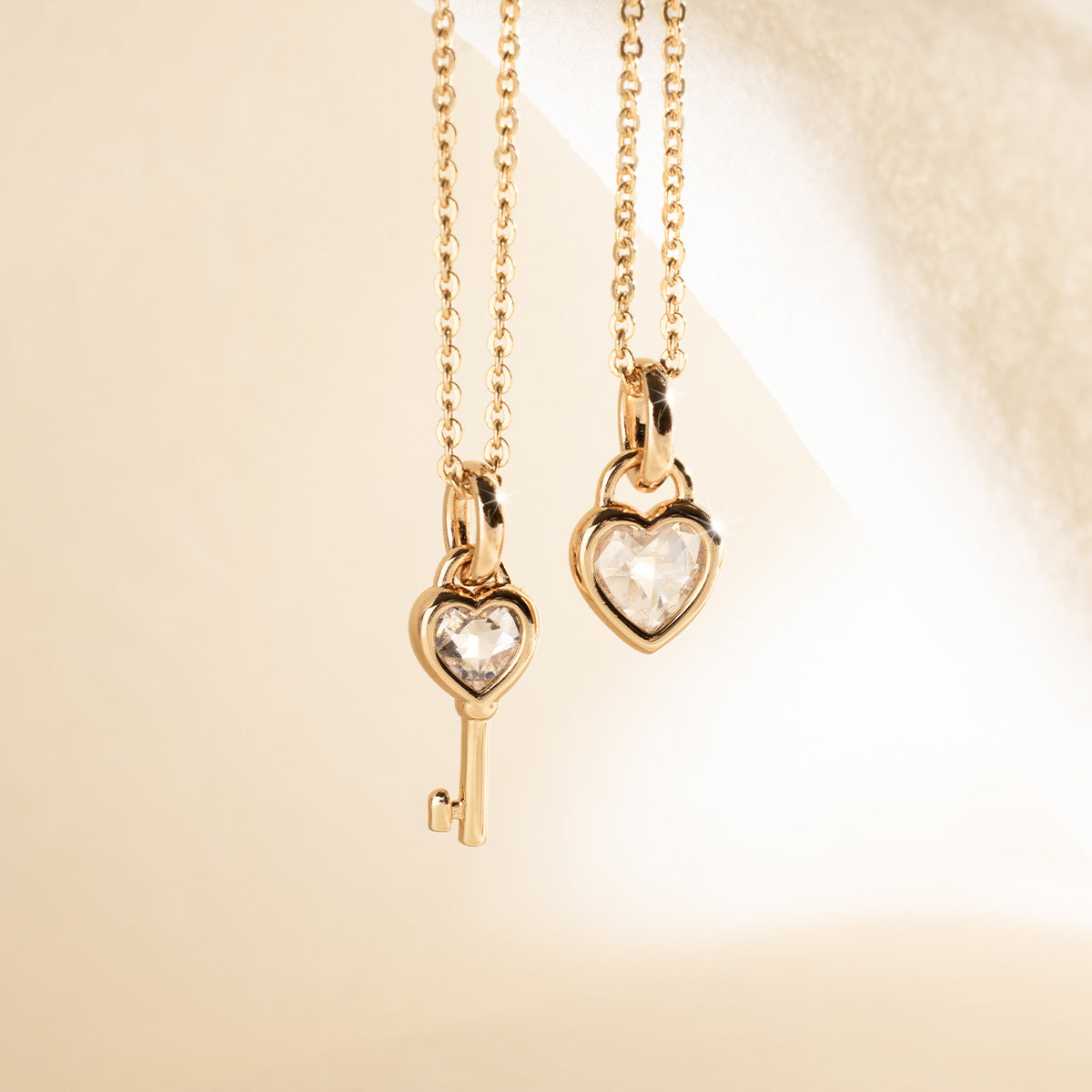 Two gold necklaces with heart and key pendants on a beige background