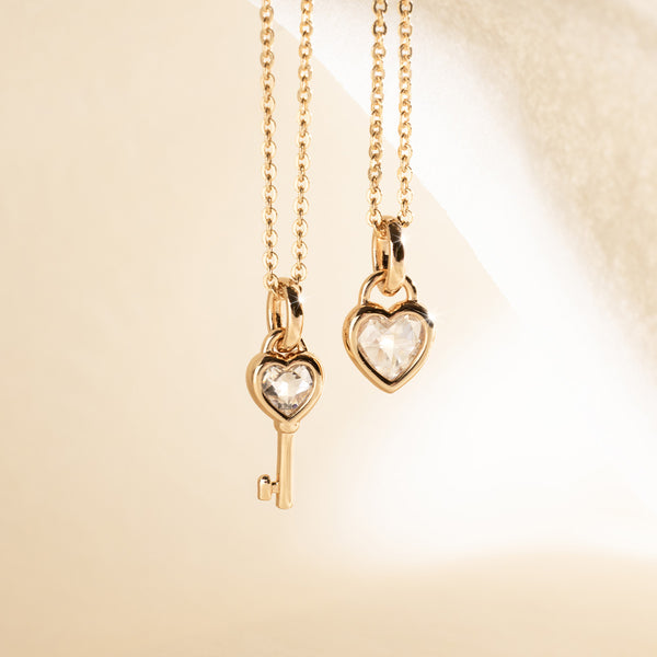 Two gold necklaces with heart and key pendants on a beige background
