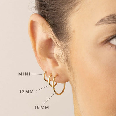 A person's ear wearing three thin gold hoops in different sizes, with text on the screen pointing to each with the sizes 'MINI', '12MM', and '16MM'.