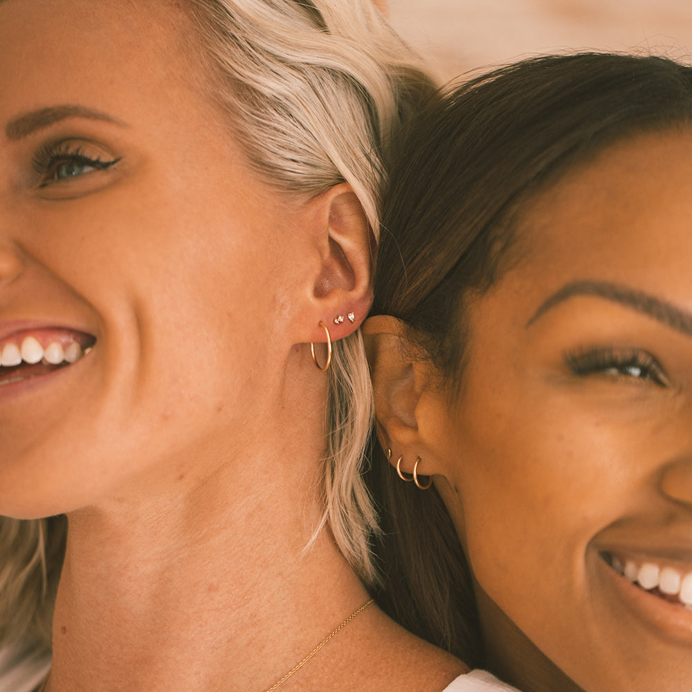 Two smiling woman wearing multiple gold earrings.