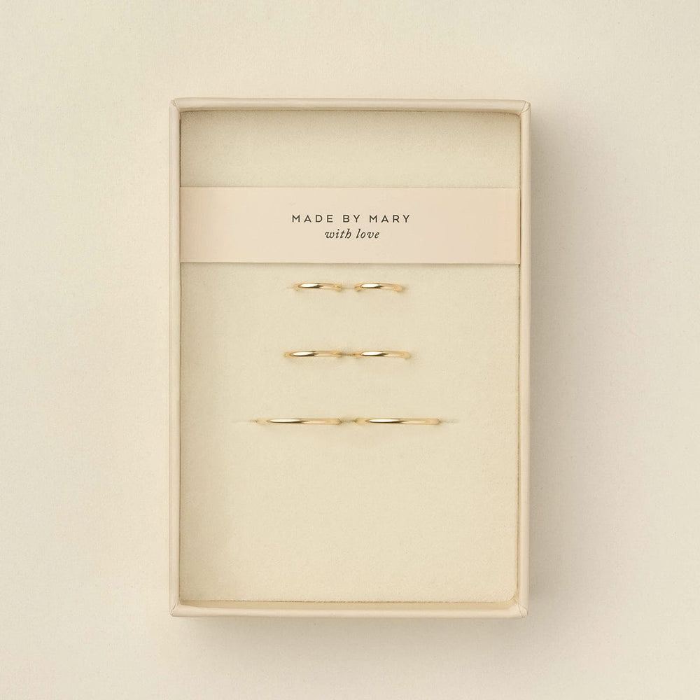 Six delicate gold wire  hoop earrings displayed inside a cream-colored presentation box with a paper band reading 'MADE BY MARY with love'.