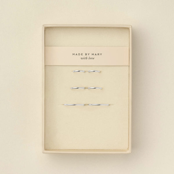 Six delicate silver wire hoop earrings displayed inside a cream-colored presentation box with a paper band reading 'MADE BY MARY with love'.