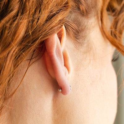 A close-up of a person's ear from the side, showing a round silver ball backing of a stud earring.