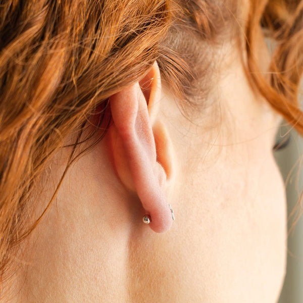 A close-up of a person's ear from the side, showing a round silver ball backing of a stud earring.