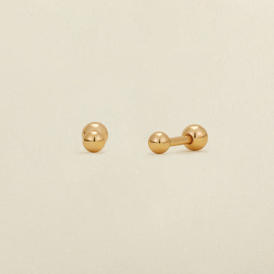 A pair of gold ball stud earrings with round ball backings, shown on a plain, warm off-white background.