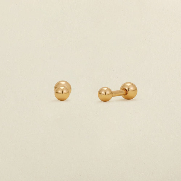 A pair of gold ball stud earrings with round ball backings, shown on a plain, warm off-white background.