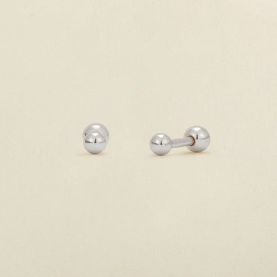 A pair of silver ball stud earrings with round ball backings, shown on a plain, warm off-white background.