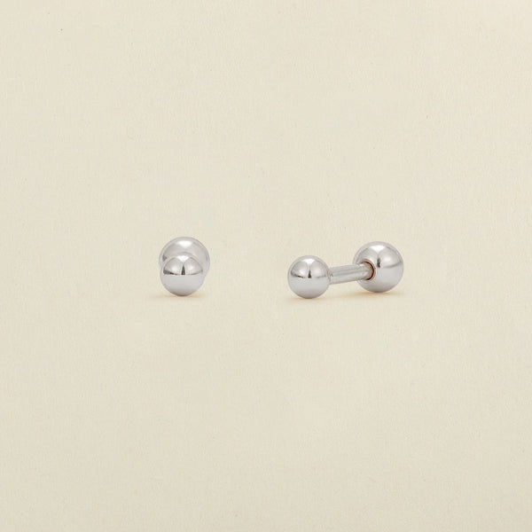 A pair of silver ball stud earrings with round ball backings, shown on a plain, warm off-white background.