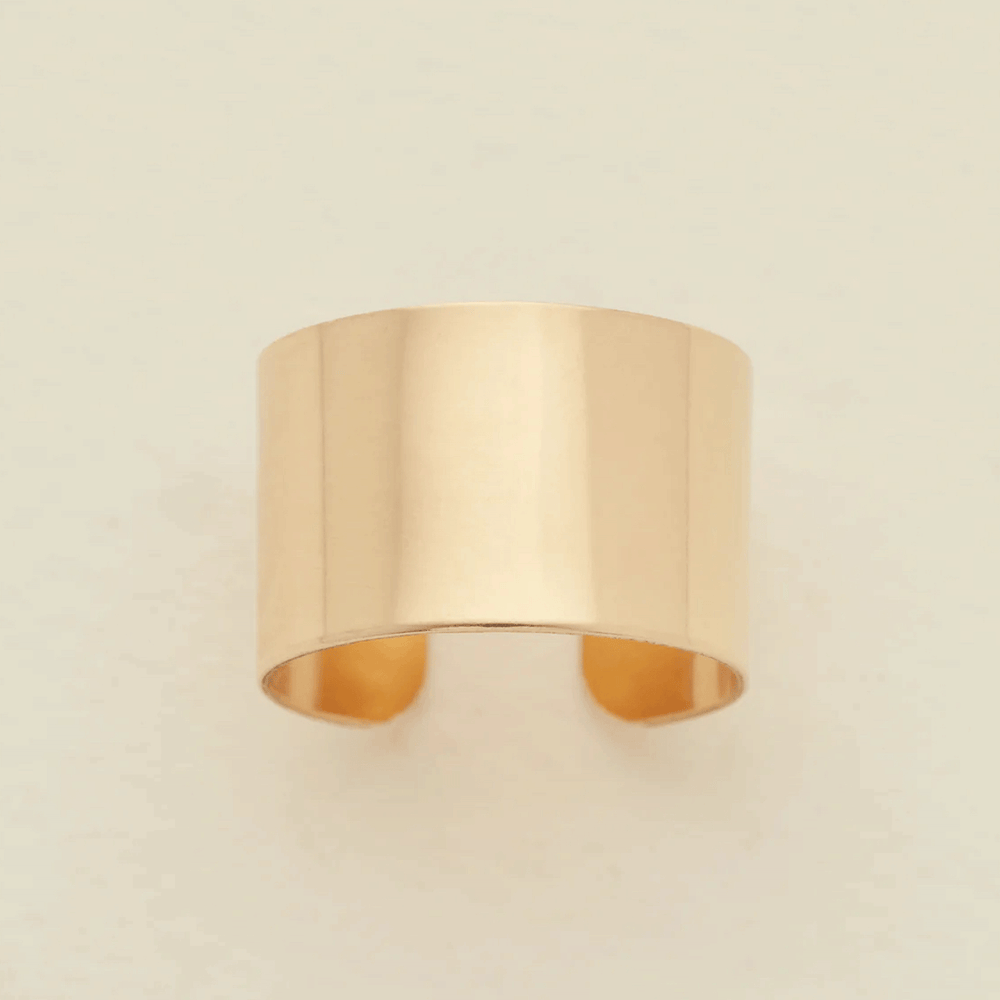 A minimalist, wide band ring in a polished gold finish, displayed against a clean, off-white background.