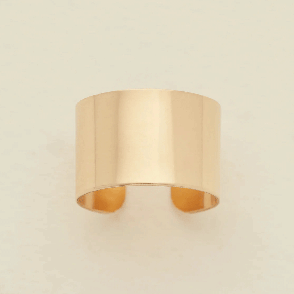 A minimalist, wide band ring in a polished gold finish, displayed against a clean, off-white background.