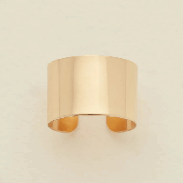 A minimalist, wide band ring in a polished gold finish, displayed against a clean, off-white background.