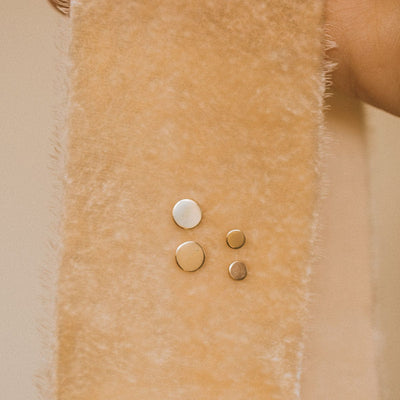 A dark beige velvet ribbon of fabric with two pairs of flat round gold disc studs pinned through it.
