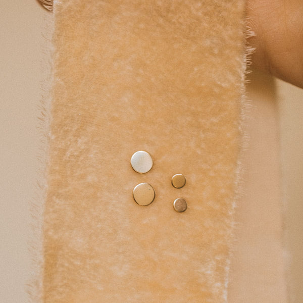 A dark beige velvet ribbon of fabric with two pairs of flat round gold disc studs pinned through it.