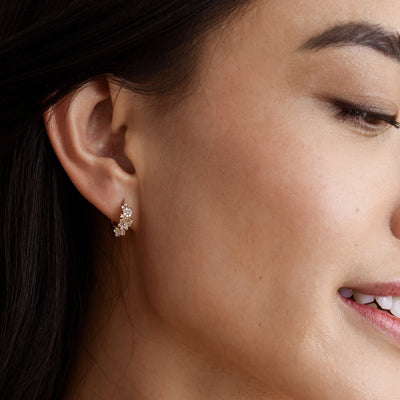 A close-up of a person's ear wearing a gold huggie hoop covered with flowers made of clear gemstones.