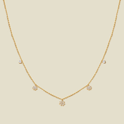 A delicate gold chain necklace with three small flowers with clear accent stones and a few tiny clear accent stones, displayed on a solid light beige background.