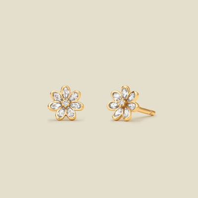 A pair of gold flower stud earrings with clear stones, displayed on a solid light beige background.
