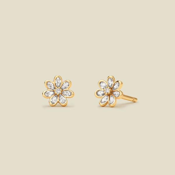 A pair of gold flower stud earrings with clear stones, displayed on a solid light beige background.