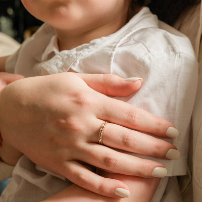 A close-up of a person's hand resting on a small child showing off two gold stacked rings, each with a different pattern of baguette and round clear stones in a morse code pattern.
