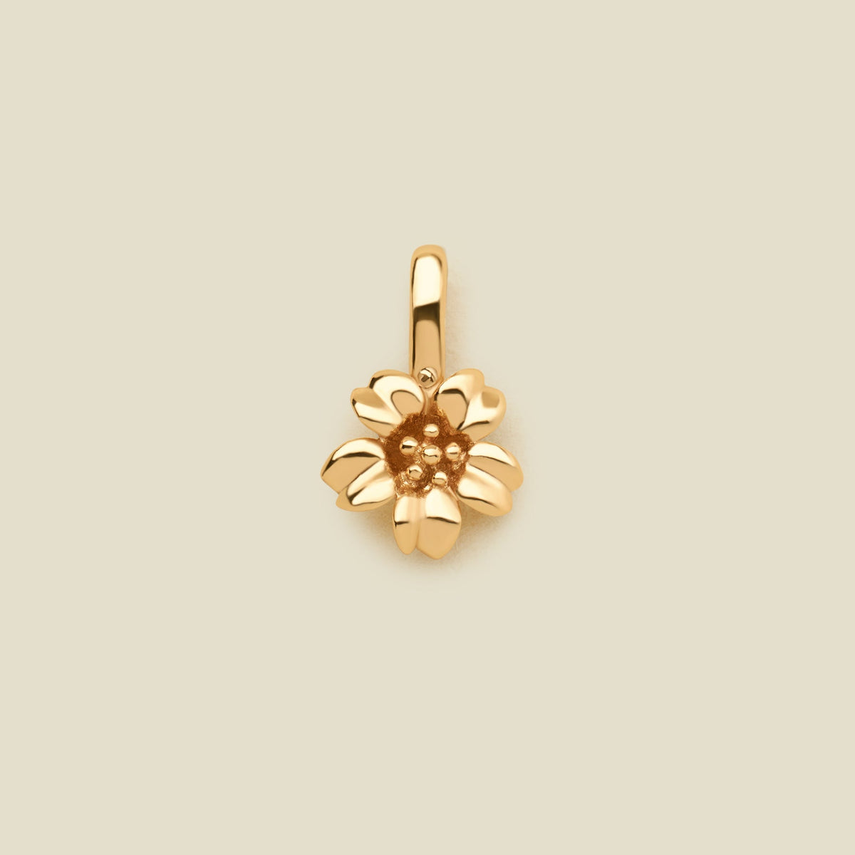 A polished gold cherry blossom flower charm, shown on a solid light beige surface.
