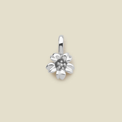 A polished silver cherry blossom flower charm, shown on a solid light beige surface.