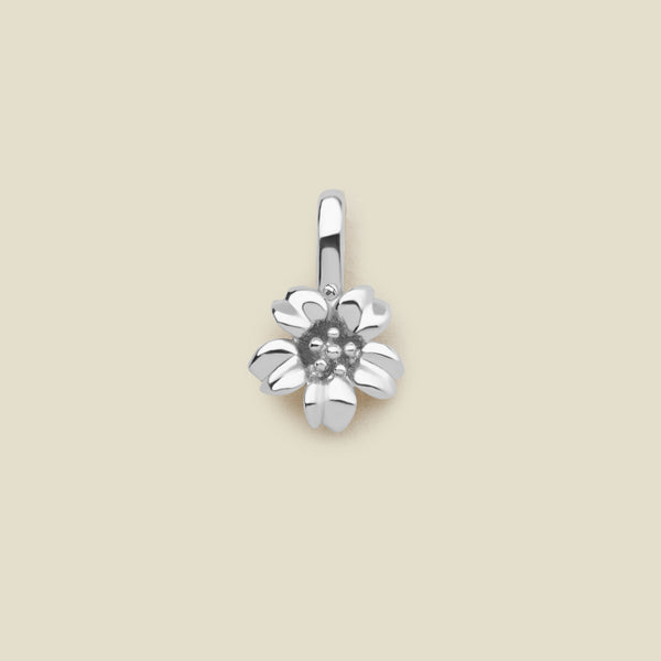A polished silver cherry blossom flower charm, shown on a solid light beige surface.